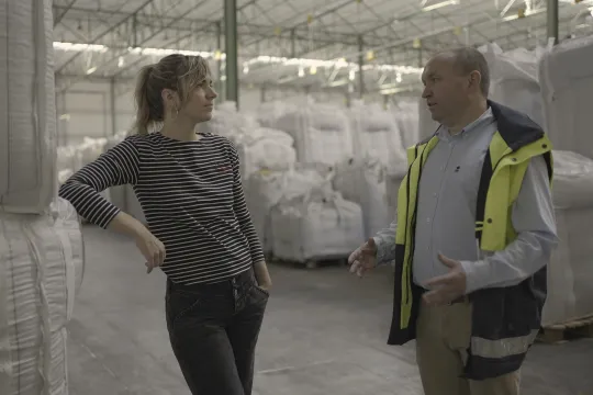 Presentator Marijn Frank praat met koffiebrander in een pakhuis met grote witte balen koffie