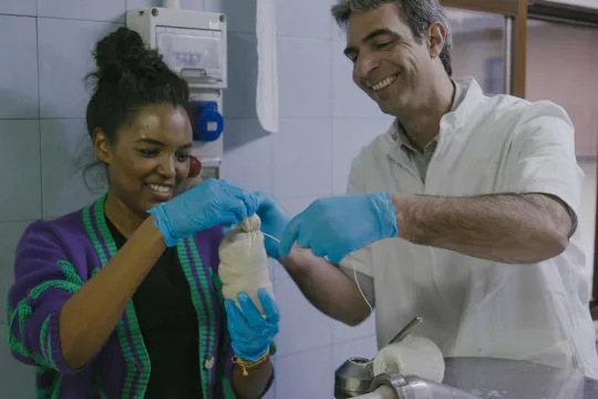 Verslaggever Sosha Duysker houdt een worst vast, met rechts van haar een kok