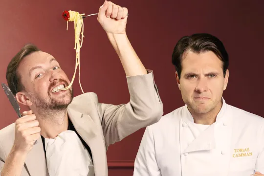 Man eet spaghetti naast man in koksschort die serieus kijkt