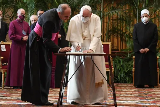 Pope Francis (C) signs a document as Egyptian Islamic scholar and the current Grand Imam of al-Azhar mosque, Sheikh Ahmed Al-Tayeb (4thR Rear) and other religious leaders stand by during the meeting "Faith and Science: Towards COP26" on October 4, 2021 in The Vatican, sending an appeal to participants in the 26th United Nations Climate Change Conference, also known as COP26, scheduled from November 1 to 12 in Glasgow, Scotland.  ALESSANDRO DI MEO / POOL / AFP