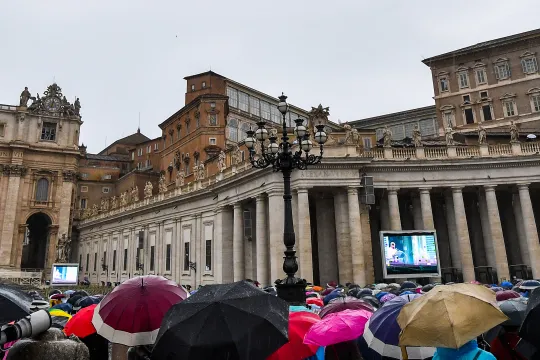 People protect themselves from the rain with an umbrella, as Pope Francis (Top R) speaks from the window of the Apostolic palace overlooking St. Peter's Square during the weekly Angelus prayer in The Vatican on September 27, 2020. Tiziana FABI / AFP