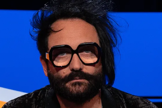 Man met zwart haar, baard en bril in studiostoel