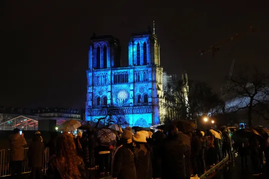 Crowds stand outside Notre-Dame Cathedral as it is illuminated during a ceremony to mark the re-opening of the landmark Cathedral, in central Paris, on December 7, 2024. Around 50 heads of state and government are expected in the French capital to attend the ceremony marking the rebuilding of the Gothic masterpiece five years after the 2019 fire which ravaged the world heritage landmark and toppled its spire. Some 250 companies and hundreds of experts were part of the five-year restoration project at a cost