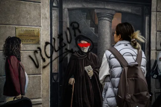 A person passes by the famous Lyonnais fresco by CiteCreation with a tag depicting the Abbe Pierre with the word "rapist" next to it, in Lyon central-eastern France, on September 30, 2024. JEFF PACHOUD / AFP