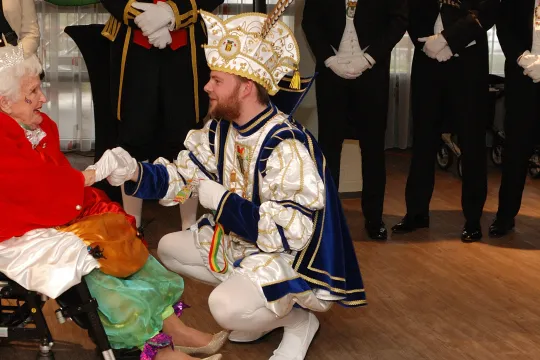 Mevrouw in rolstoel omringd door mannen in carnavalspakken