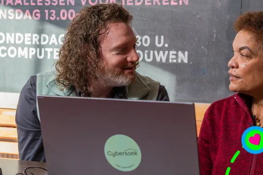 Twee mensen achter een laptop kijken elkaar aan
