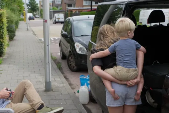 Man zit naast open bus met meisje met kind op rug