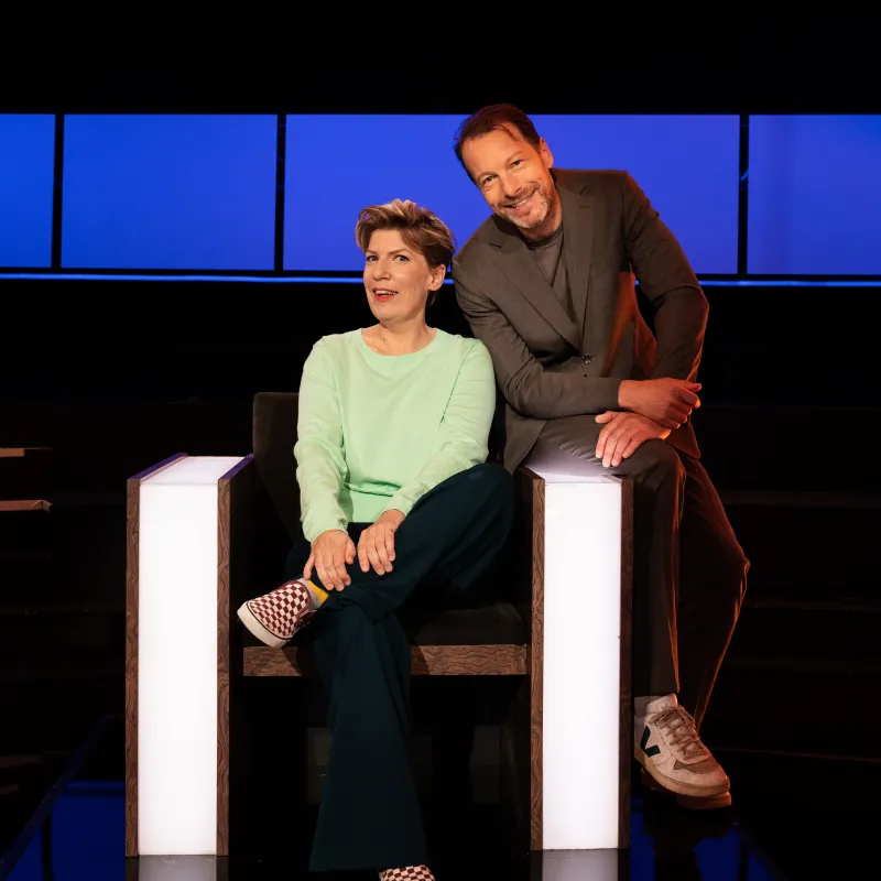 Vrouw zit in stoel met man op de leuning in een studio