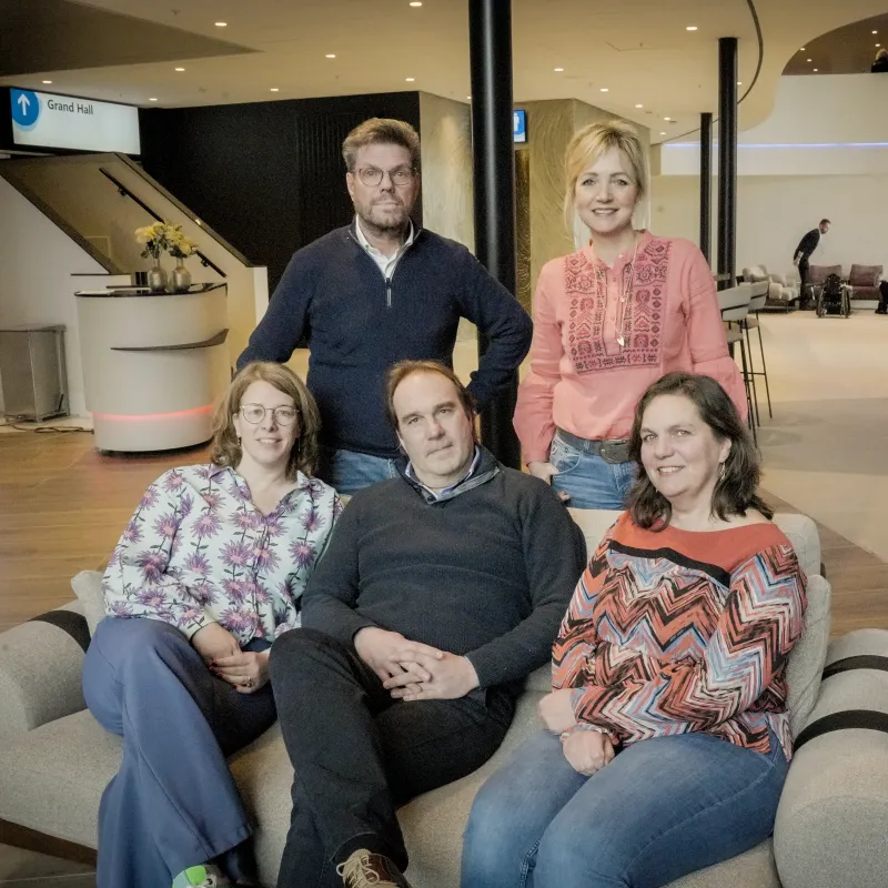 Drie mensen zitten op een bank en twee mensen staan erachter