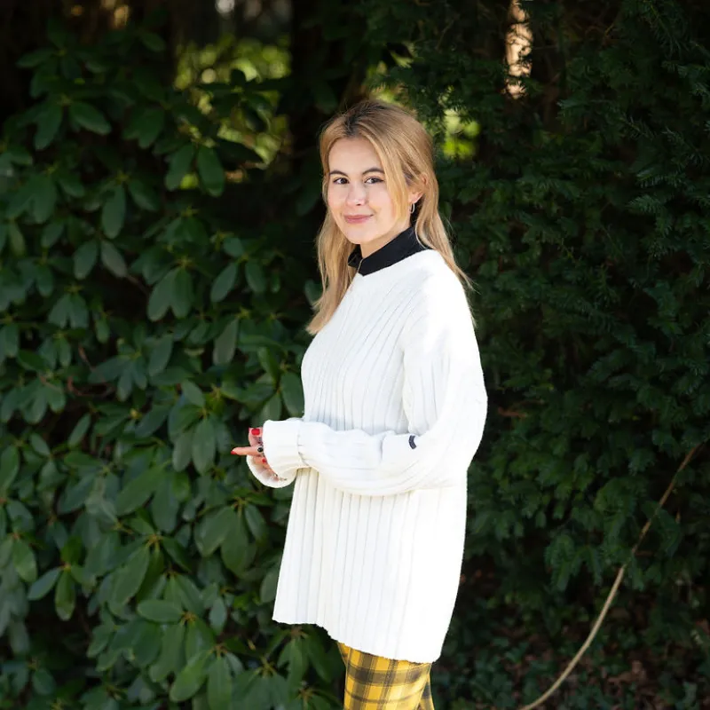 Blonde jonge vrouw met witte trui voor een grote struik