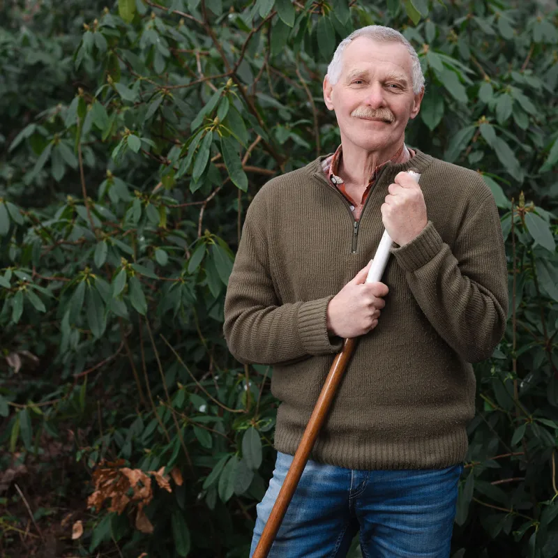 Een volwassen man houdt een schoffel vast 