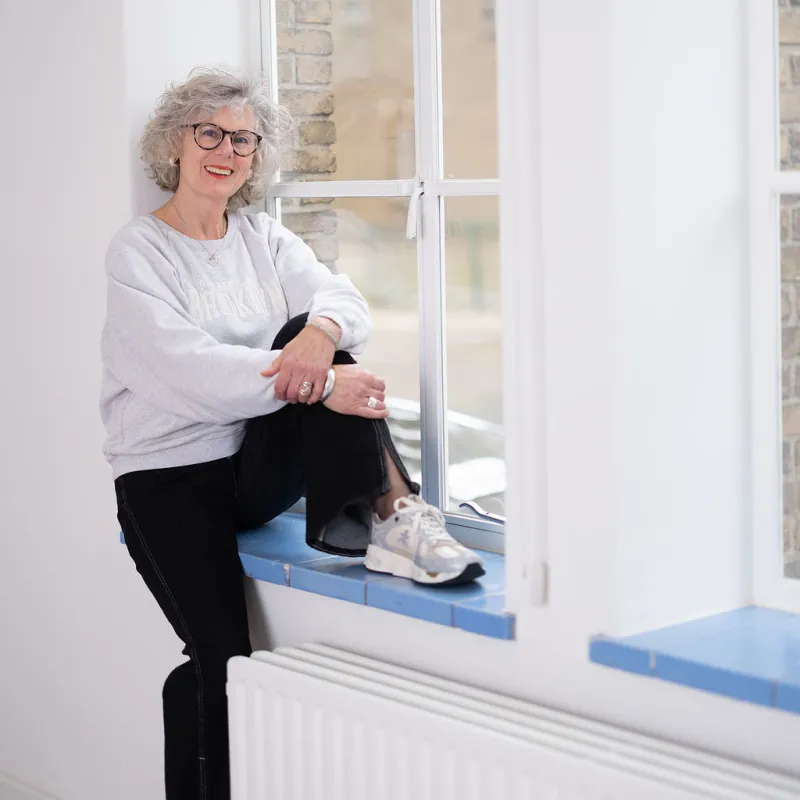 Volwassen vrouw met grijze trui zit in het raamkozijn