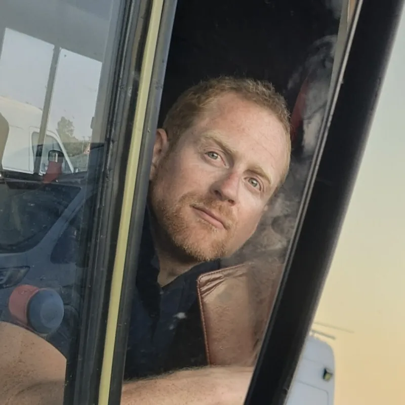 Vanlifer kijkt vanuit het raam van zijn camper de camera in