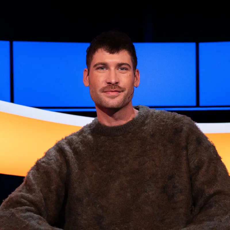 Man met bruin haar en snor en bruine trui