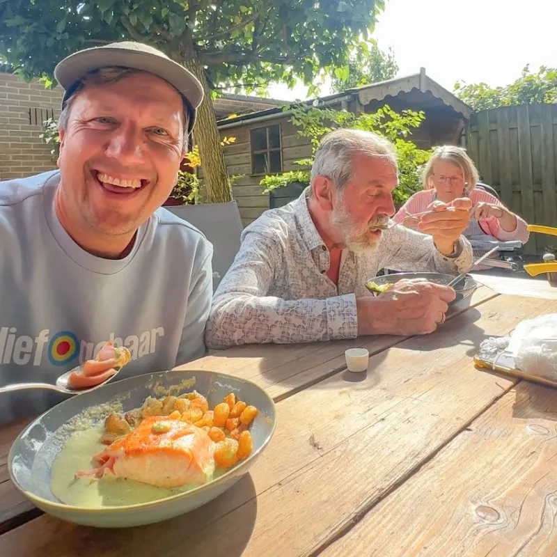 Lachende man met pet eet met oudere man en vrouw