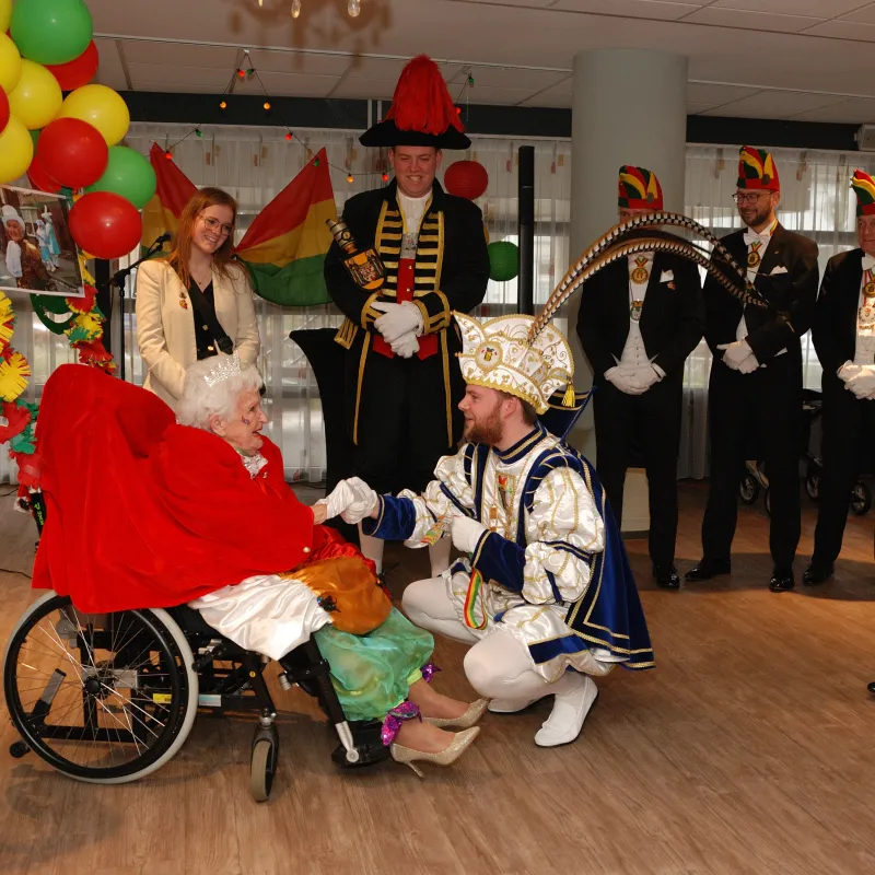 Mevrouw in rolstoel omringd door mannen in carnavalspakken