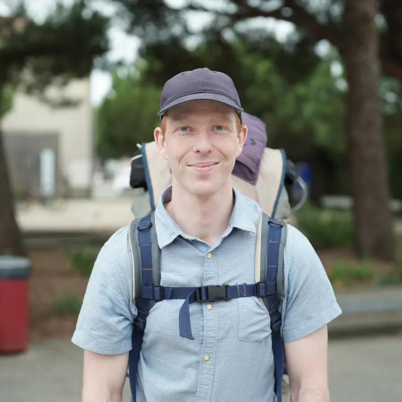 Man met pet en rugzak in blauwe blouse met korte mouwen