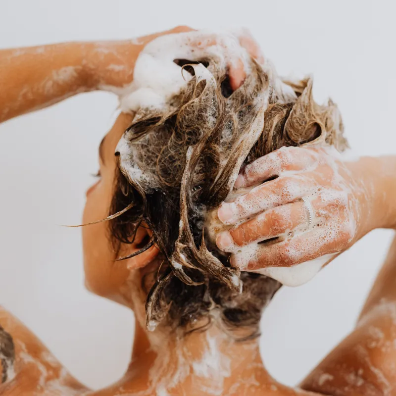 Een vrouw onder de douche die haar haren wast met shampoo