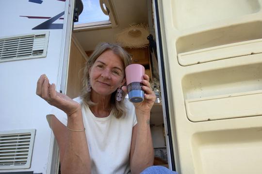 Onderweg naar liefde - Lotty Vrouw zit in de deuropening van een camper en kijkt vriendelijk de camera in