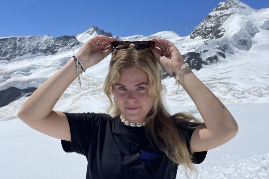 Onderweg naar liefde - Silke Vrouw houdt zonnebril vast op haar hoofd met op de achtergrond sneeuwgebied