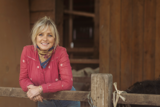 een vrouw met roze blouse poseert in een stal