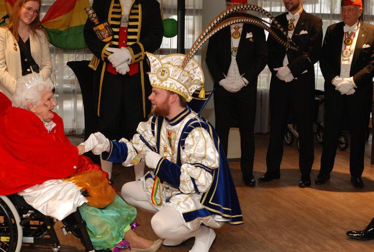 Mevrouw in rolstoel omringd door mannen in carnavalspakken