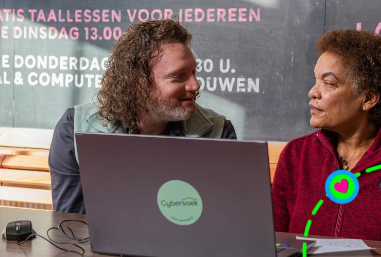 Twee mensen achter een laptop kijken elkaar aan