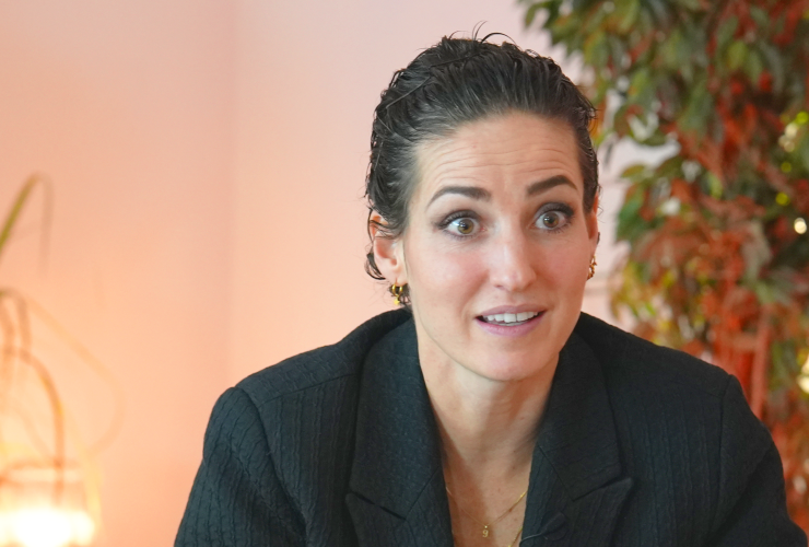 Myrthe Schoot zit in een zwart pak, heeft een mok in haar hand en is iets aan het vertellen