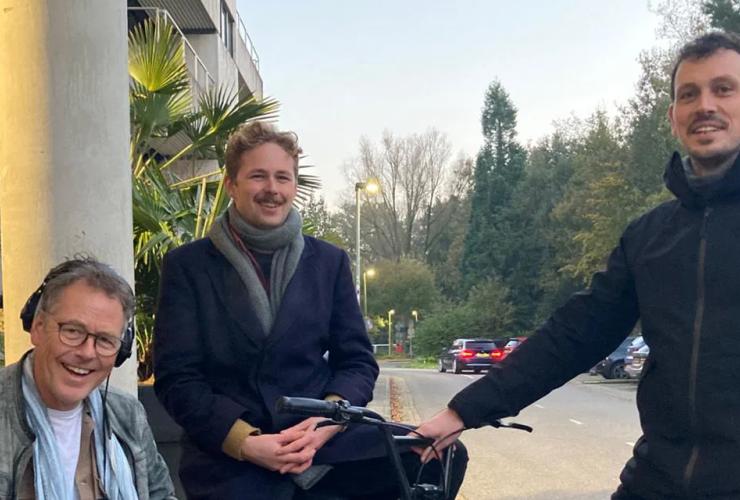 Een fiets met zijspan met twee mannen erin met een man ernaast