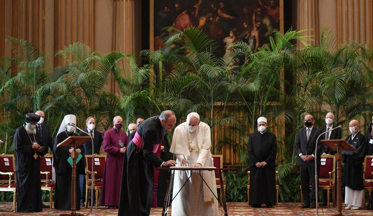 Pope Francis (C) signs a document as Egyptian Islamic scholar and the current Grand Imam of al-Azhar mosque, Sheikh Ahmed Al-Tayeb (4thR Rear) and other religious leaders stand by during the meeting "Faith and Science: Towards COP26" on October 4, 2021 in The Vatican, sending an appeal to participants in the 26th United Nations Climate Change Conference, also known as COP26, scheduled from November 1 to 12 in Glasgow, Scotland.  ALESSANDRO DI MEO / POOL / AFP
