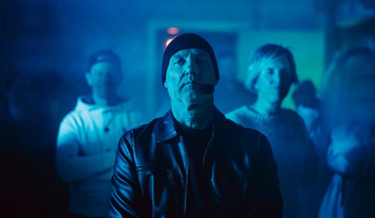 Man met muts op kijkt serieus de camera in blauw licht 