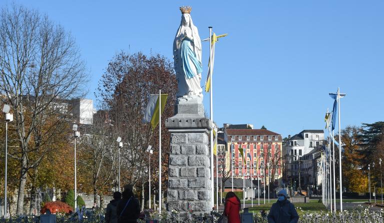 Pedestrian stand in front of a statue of the Virgin Mary in Lourdes, southwestern France,