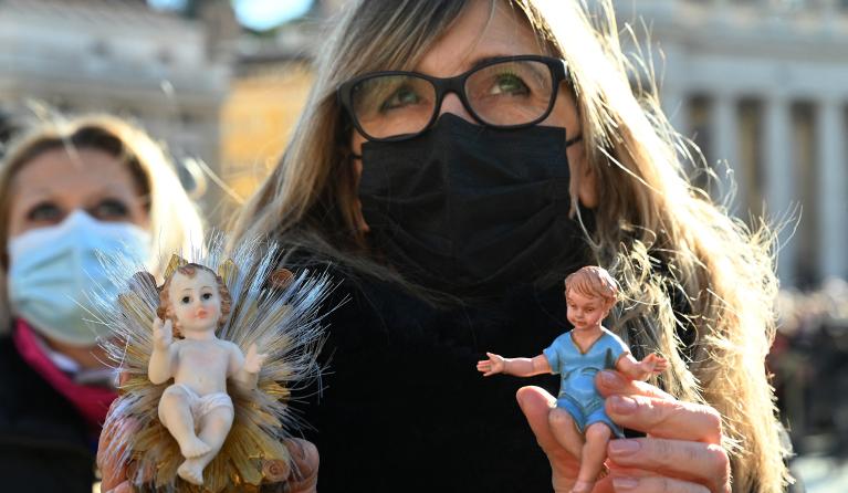 A woman holds up Nativity Scene figurines of baby Jesus during the traditional blessing of figurines as part of the pope's Sunday Angelus prayer before Christmas in Saint Peter's square at the Vatican on December 12, 2021.