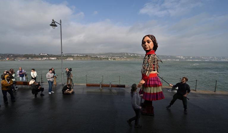 'Little Amal', a giant puppet depicting a Syrian refugee girl, walks along the sea front at the harbour in Folkestone, south east England, on October 19, 2021 after arriving from Calais, as part of the international art project The Walk. 'Little Amal' was designed by The Handspring Puppet Company and represents a Syrian refugee child and the millions of displaced children worldwide. 'Little Amal' is making a 8000 km journey across Europe to the United Kingdom