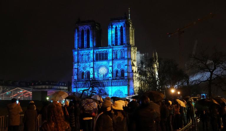 Crowds stand outside Notre-Dame Cathedral as it is illuminated during a ceremony to mark the re-opening of the landmark Cathedral, in central Paris, on December 7, 2024. Around 50 heads of state and government are expected in the French capital to attend the ceremony marking the rebuilding of the Gothic masterpiece five years after the 2019 fire which ravaged the world heritage landmark and toppled its spire. Some 250 companies and hundreds of experts were part of the five-year restoration project at a cost