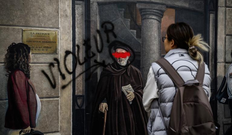 A person passes by the famous Lyonnais fresco by CiteCreation with a tag depicting the Abbe Pierre with the word "rapist" next to it, in Lyon central-eastern France, on September 30, 2024. JEFF PACHOUD / AFP