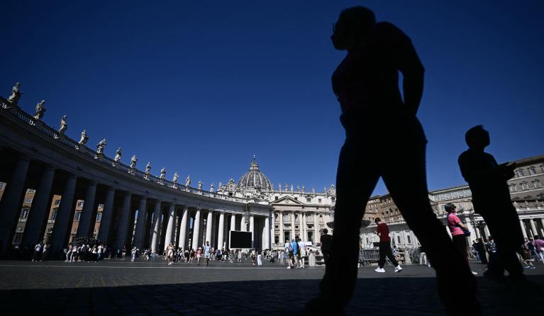 A visitor stands silhouetted with the colonnade (L) and the St Peter's Basilica in the background, following the funeral of the Pope and ahead of the conclave, at St Peter's Square in The Vatican, on May 2, 2025. The conclave begins on May 7, when a record 133 cardinals -- those under the age of 80 who are eligible to vote -- will enter the Sistine Chapel to vote in secret for a new pontiff.  Filippo MONTEFORTE / AFP