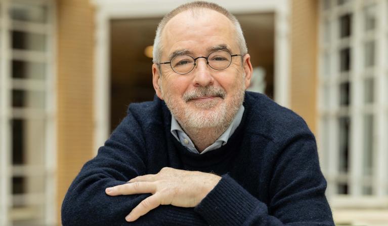 Man met bril glimlacht steunend op een stapel boeken