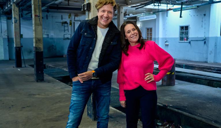 Klaas van Kruistum met blauw overhemd en jeans naast Irma Sluis in roze shirt en zwart broek in een lege fabriekshal