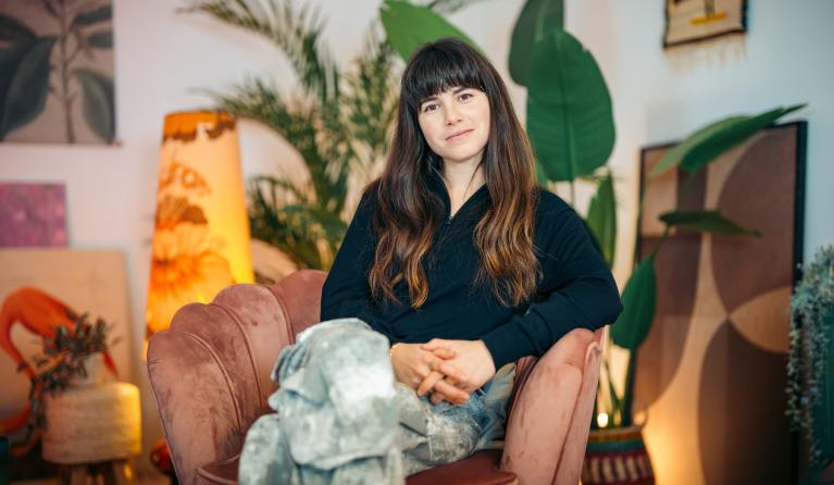 Hanna van Vliet zit met haar benen over elkaar in een stoel en kijkt glimlachend de camera in