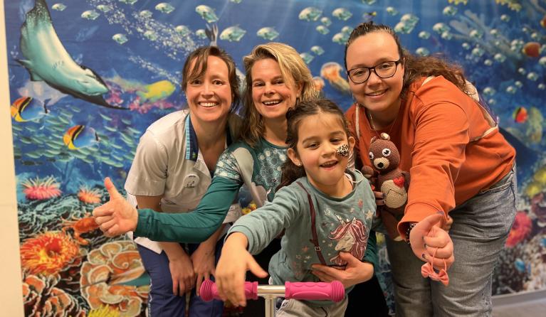 Een ziek kindje poseert in het ziekenhuis met haar moeder en verplegend personeel