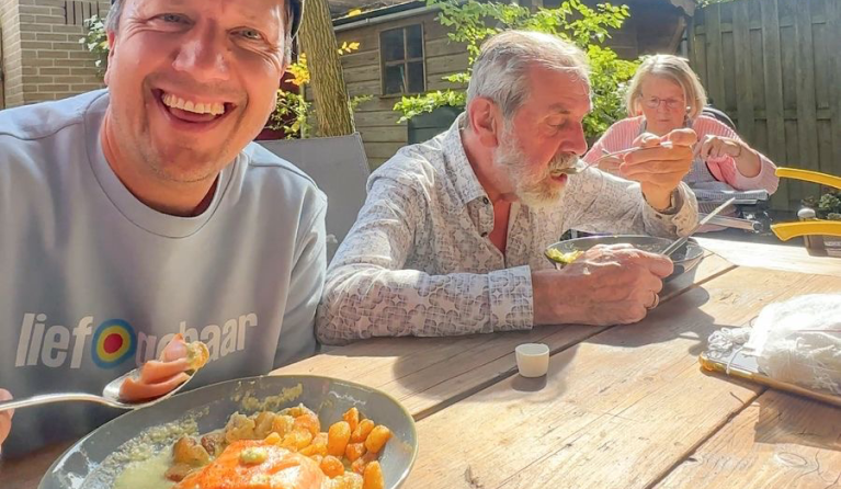 Lachende man met pet eet met oudere man en vrouw