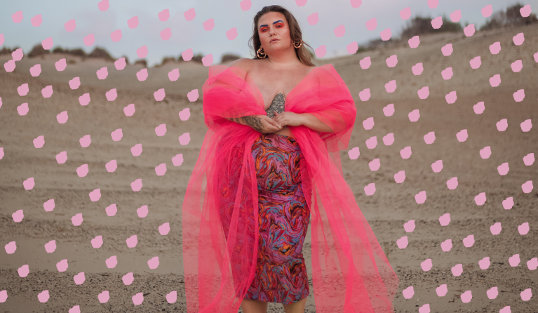 Lotte van Eijck, een prachtige curvy vrouw, staat krachtig in het midden van een zandvlakte in een roze jurk.