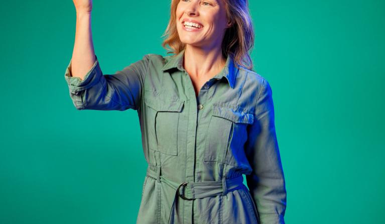 Marieke Schatteleijn poseert voor een groene achtergrond met een hand omhoog