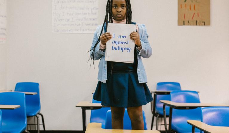een meisje staat op een stoel met een bordje in haar hand waarop staat dat ze tegen pesten is