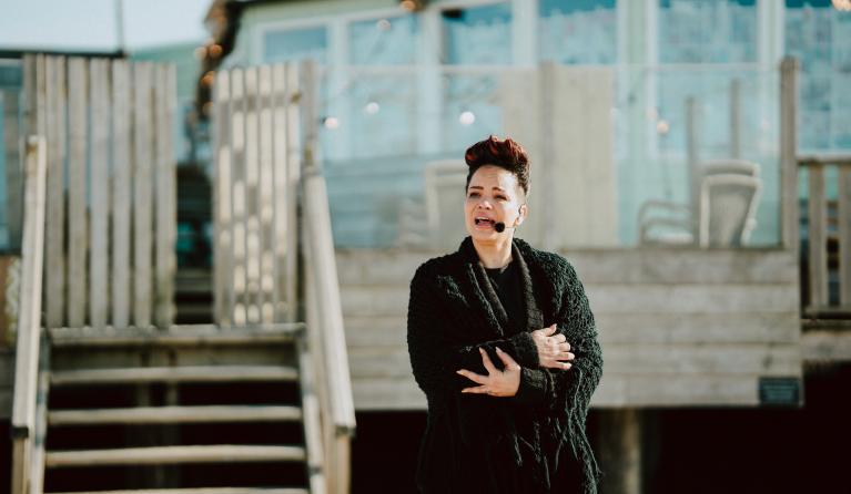Vrouw staat voor een strandhuis te zingen