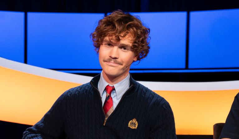 Man met krullen en blauw vest met stropdas