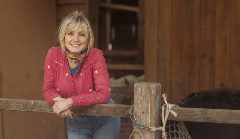 een vrouw met roze blouse poseert in een stal