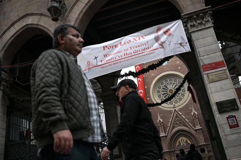 Pedestrians walk past the Saint Anthony of Padua Church as a welcome banner bearing a portrait of Pope Leo XIV is displayed on its gate, ahead of his visit to Turkey, in Istanbul on November 24, 2025. Ozan KOSE / AFP