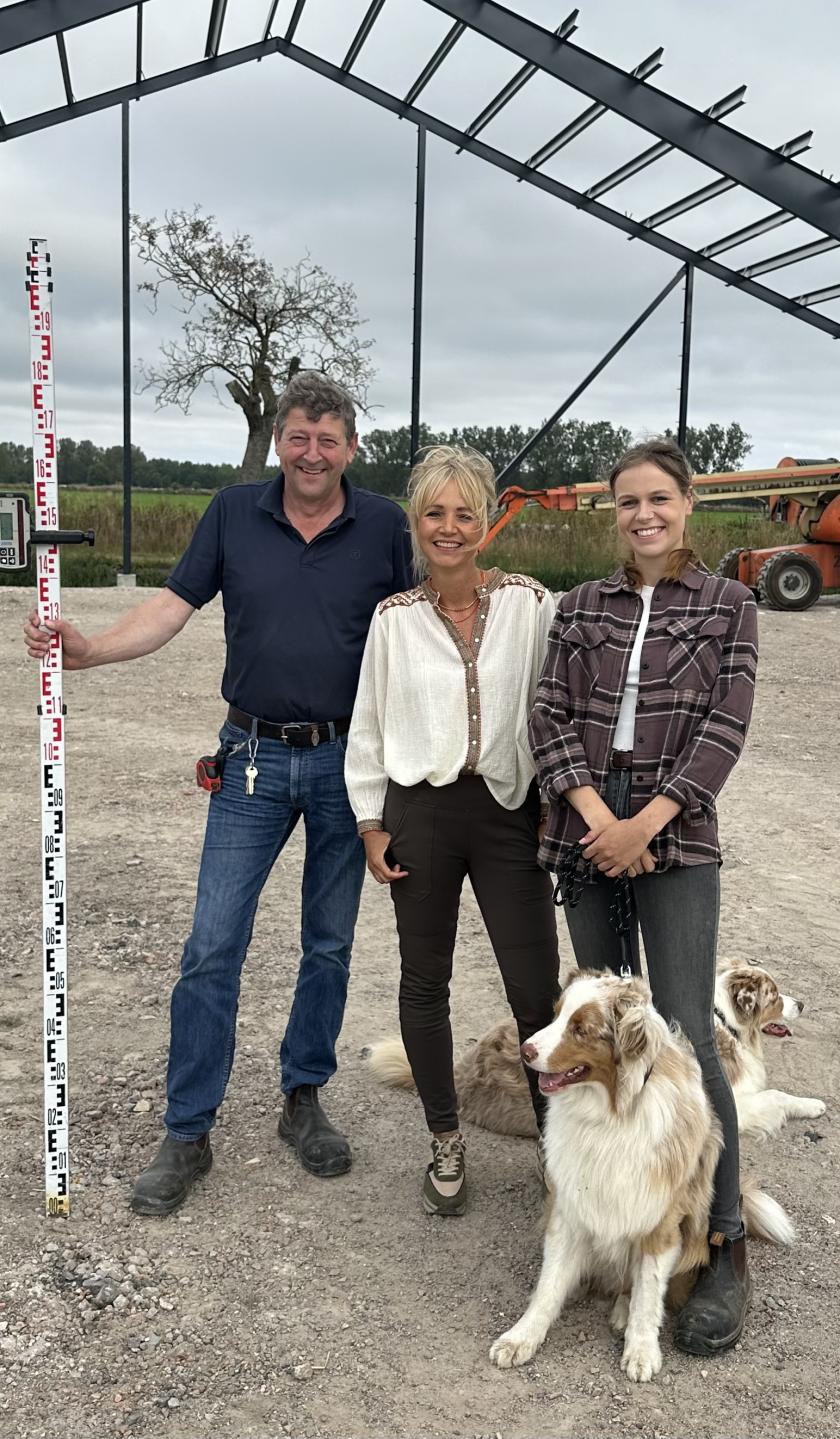 drie mensen poseren voor een opslagschuur in aanbouw